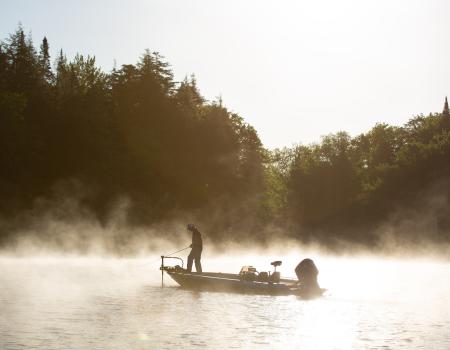 A angler fishing off a boat in the morning mist.