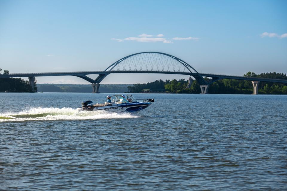 Two men ride in a boat on the lake with a bridge in the background.