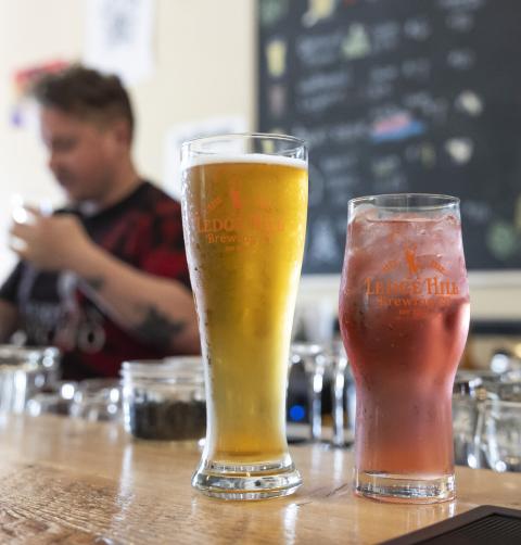 A beer and a cocktail sit on a sunny wooden bar