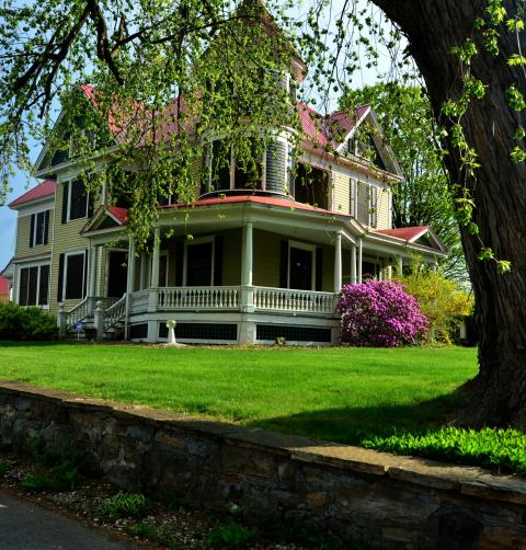 A victorian era home with red roof and a giant willow tree. 