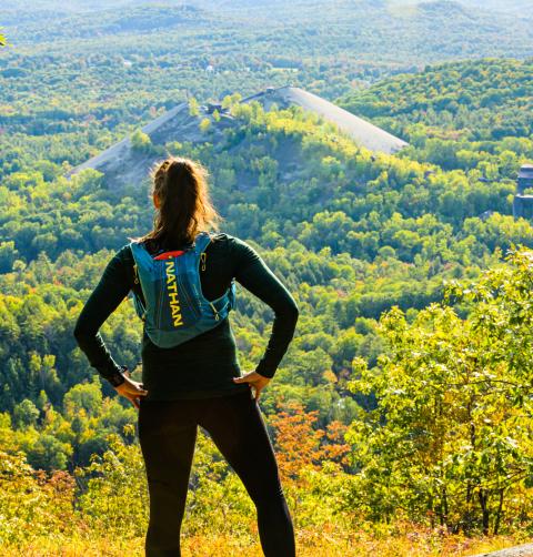 A woman looks out to a green mountain range during sunset. 