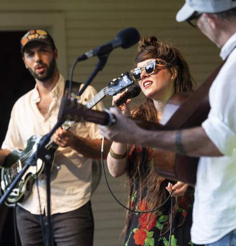 A woman and two men sing a concert with guitars. 