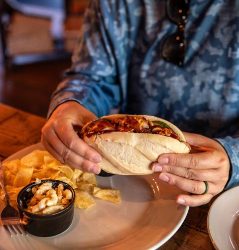 A woman holds a sandwich with a side of chips and mac and cheese. 