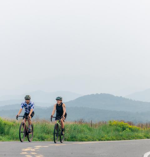 Two people cycling down a road during the summer in the Lake Champlain Region.