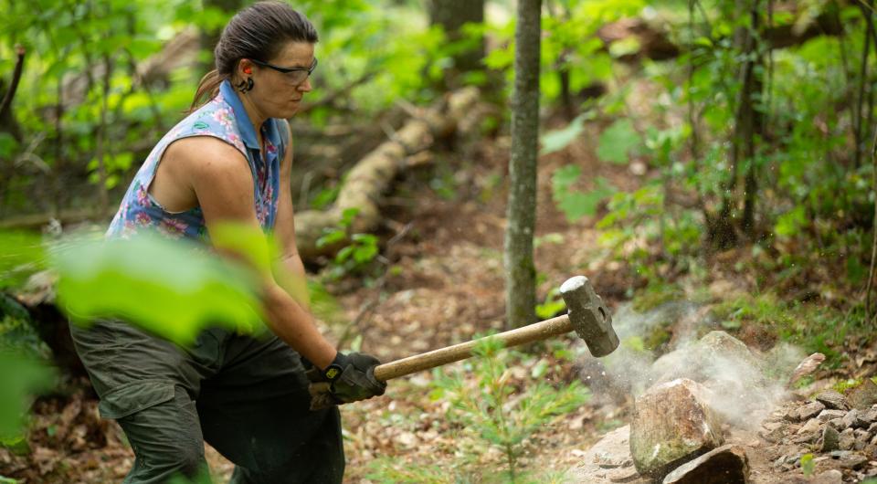 A woman breaks up a stone with a large hammer