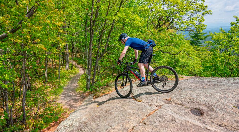 A mountain biker goes down a rock slab towards a single track trail