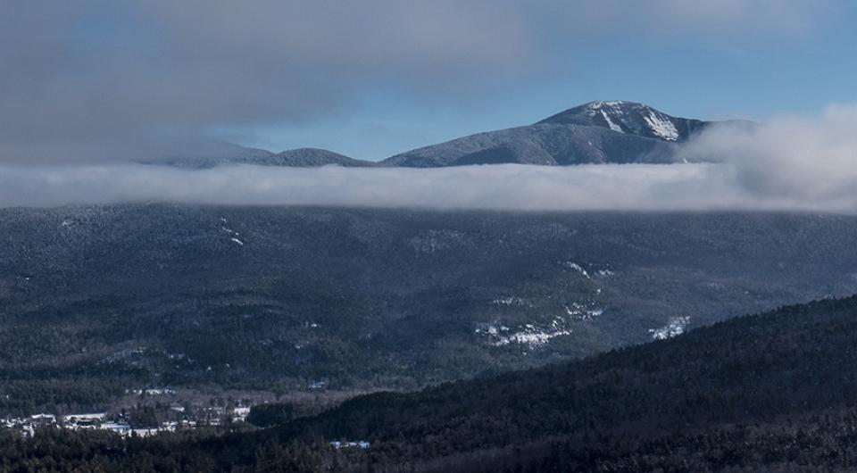 A tall mountain pokes through clouds in the winter