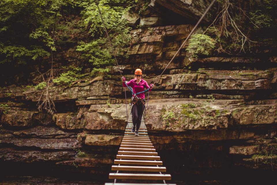 A woman walks across a high ropes course over a chasm