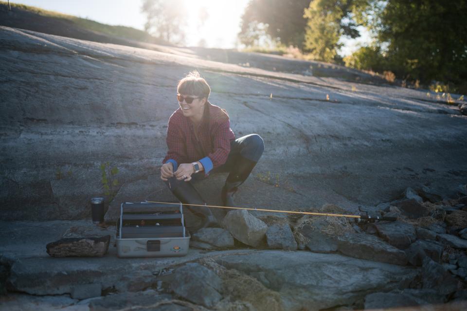 An angler kneels near their tackle box on the rocky shore