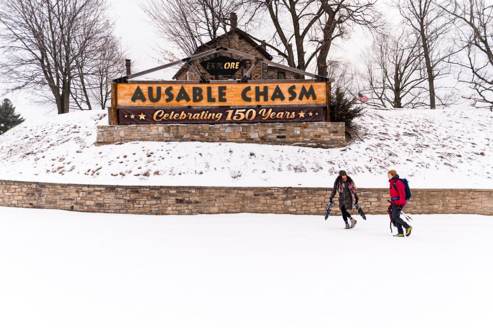 Two people walking in the snow in from of the Ausable Chasm sign