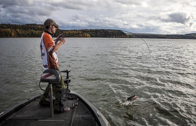 A fisherman reels in a catch from the bow of a low fishing boat.