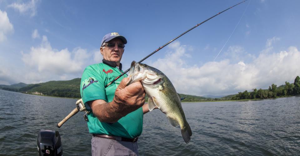 A fisherman holds up a fresh catch from a lake.