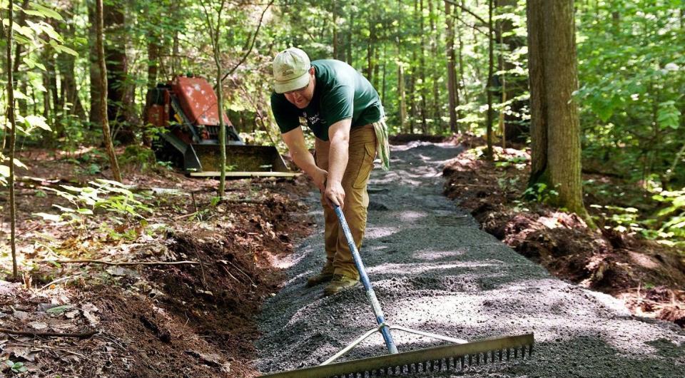 A man rakes a trail of stone through the woods