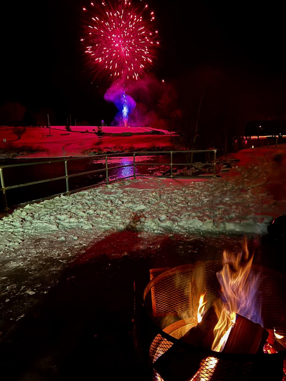 A fire close by as fireworks go off in the distance