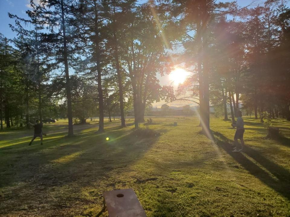 Two boys play catch in front of a sunset in the park.