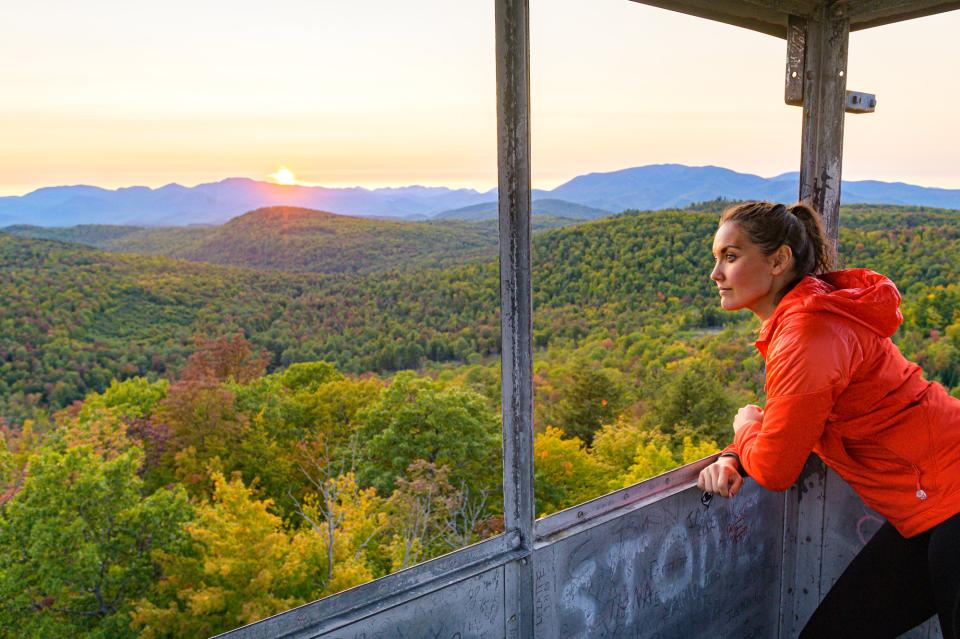 A woman looks out a fire tower to fall foliage.