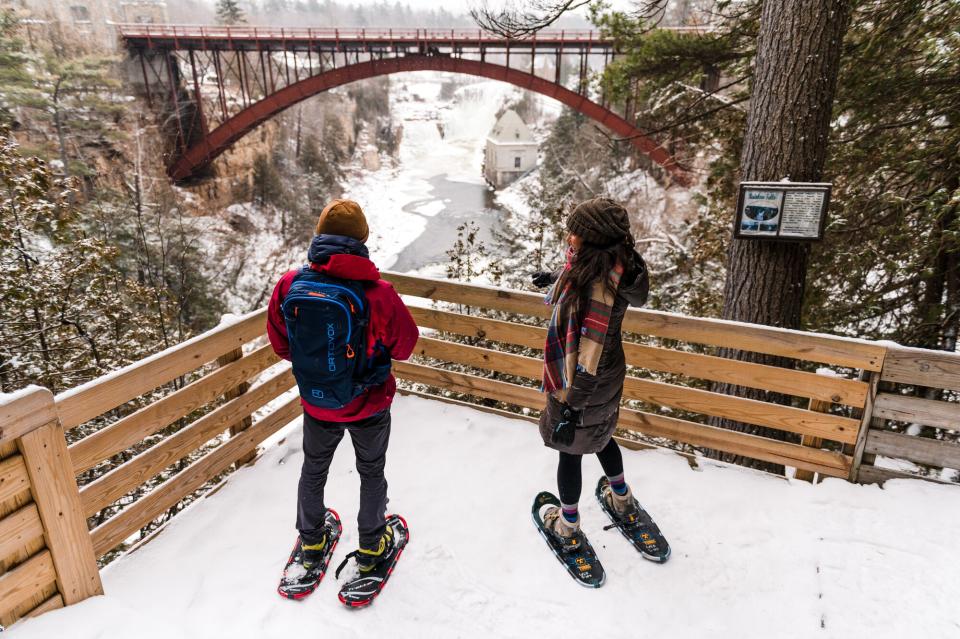 Two people in snowshoes look at an icy chasm