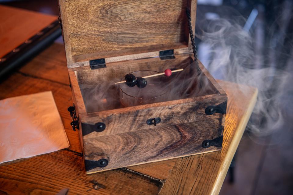 An alcoholic beverage with smoke in a wooden box