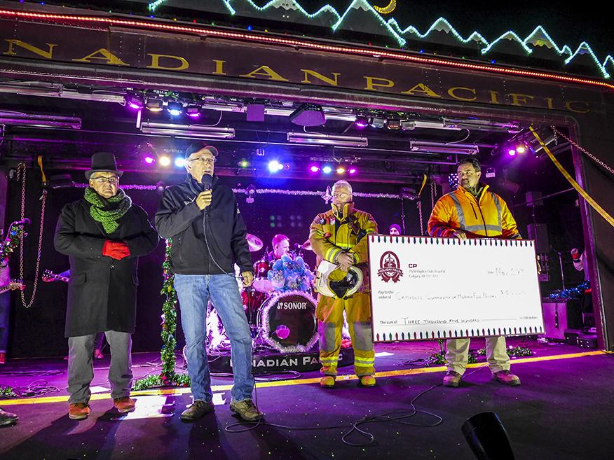 A group of men in a train car show a large check for charity to a crowd.