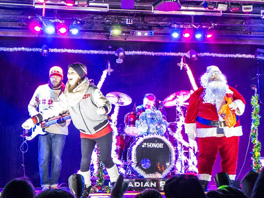 A woman sings to a crowd with santa.